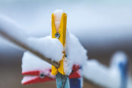 Colorful clips for washing laundry covered with snow on strip rope outdoor. Winter housework concept, close up, shallow depth of the field.の写真素材
