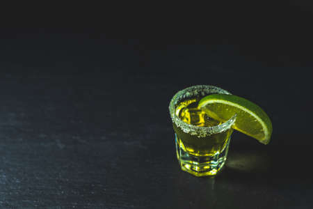 Mexican Gold Tequila shot with lime and salt on black stone table surface, selective focus, shallow depth of the field, copy space.の写真素材