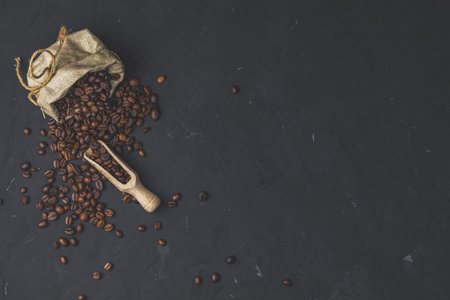Purse with roasted beans and wooden scoop on black stone concrete textured surface background. Top view with copy space for your text.の写真素材