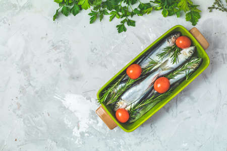 Sardines or baltic herring with tomatoes, parsley and rosemary on green dish on light gray concrete table surface. Raw uncooked sea fish, top view, copy space for you text, flat layの写真素材