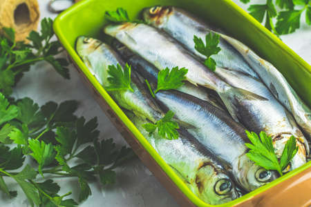 Sardines or baltic herring on green dish with parsley on light gray concrete table surface. Raw uncooked sea fish.の写真素材