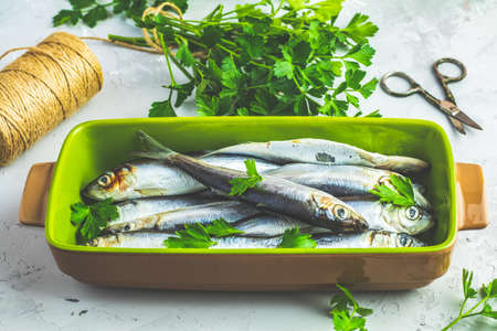 Sardines or baltic herring on green dish with parsley on light gray concrete table surface. Raw uncooked sea fish.の写真素材