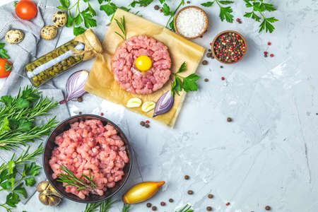 Healthy food, cooking concept. Homemade raw organic minced beef meat and steak tartare with yolk with vegetables on light gray stone concrete textured surface background. Copy space background, top view flat lay.の写真素材