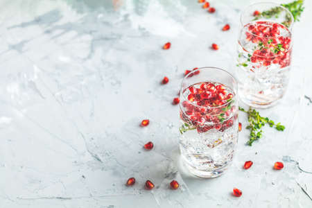Festive drinks, gin and tonic pomegranate cocktail or detox water with ice. Selective focus, copy space for text, light gray concrete table surface.の写真素材