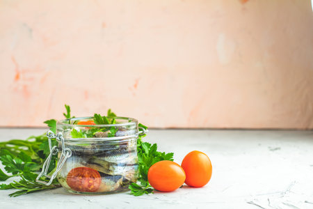 Sardines or baltic herring with rosemary, thyme, parsley, tomatoes slices and spaces in glass jar on...