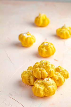 Delicious profiteroles with cream on pink or peach color concrete surface, copy space. Sweet food...