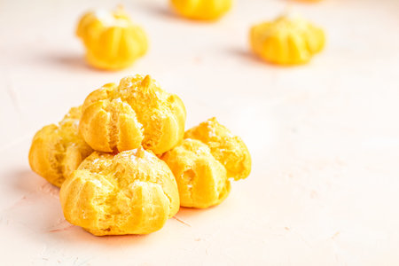 Delicious profiteroles with cream on pink or peach color concrete surface, copy space. Sweet food...