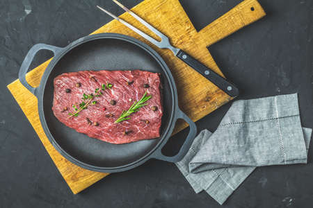 Fresh raw meat beef steak with ingredients for cooking spices, thyme and rosemary in black frying pan on dark background, top view, copy space for you text.の写真素材