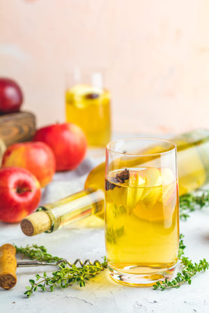 Bottle and glasses of homemade organic apple cider with fresh apples in box, light concrete table...