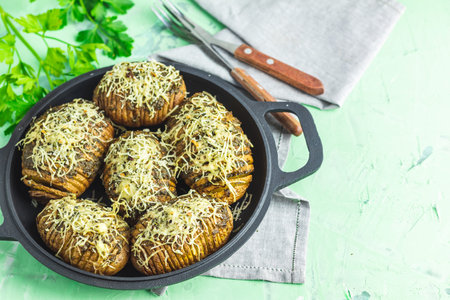 Delicious portion baked potatoes in black frying pan with pesto sauce, green onion, and cheese. Dish...