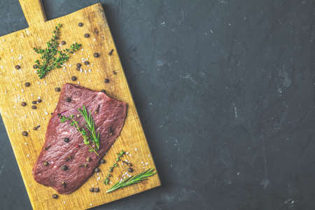 Fresh raw meat beef steak on wooden cutting board with ingredients for cooking spices, thyme, rosemary and olive oil, dark background, top view, copy space for you text.の写真素材