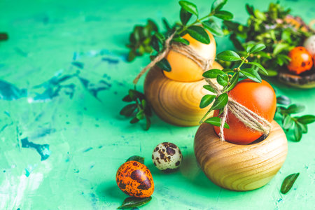 Easter concept with colored yellow orange eggs decorated green branches in wooden plate over green concrete surface background. Copy space.の写真素材