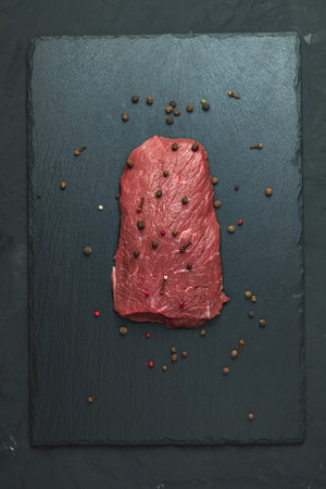 Fresh raw meat beef steak with ingredients for cooking spices, thyme on dark background, top view,...
