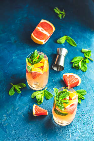 Grapefruit and fresh mint cocktail with juice, cold summer citrus refreshing drink gin tonic cocktail or beverage with ice on dark blue concrete surface.の写真素材