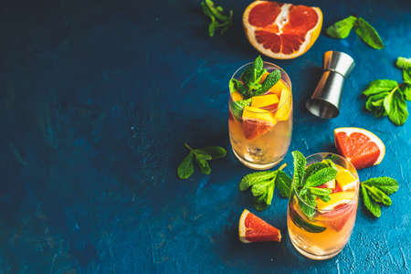 Grapefruit and fresh mint cocktail with juice, cold summer citrus refreshing drink gin tonic cocktail or beverage with ice on dark blue concrete surface.の写真素材