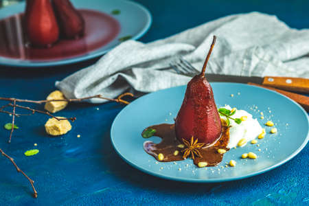 Pears in wine. Traditional dessert pears stewed in red wine with chocolate sauce on plate on blue concrete surface. Concept for romantic dinner dessertの写真素材