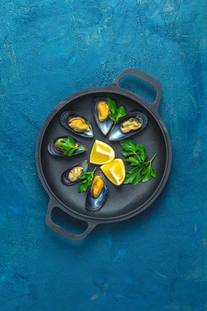 Seafood mussels with lemon and parsley in black metal pan on dark blue concrete table surface, top...