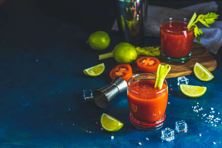 Tomato juice with celery, spices, salt and ice in portion drink glasses with copy space. Bloody Mary cocktail. Alcoholic drink and ingredients at dark blue concrete table surface.の写真素材
