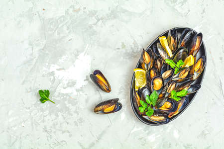 Seafood mussels with lemon and parsley in black metal plate on light gray concrete table surface, top view, copy space for you textの写真素材