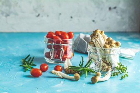Buna Shimeji - edible mushroom from East Asia. Good food for good health. Clump of shimeji mushroom and cherry tomatoes in jars on blue concrete surface backgroundの写真素材