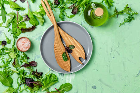 Green leaves lettuce, olive oil,  pink salt, empty ceramic bowl, wooden spoons for salad over green concrete texture background. Top view, healthy food concept, top view, copy space for you text.の写真素材