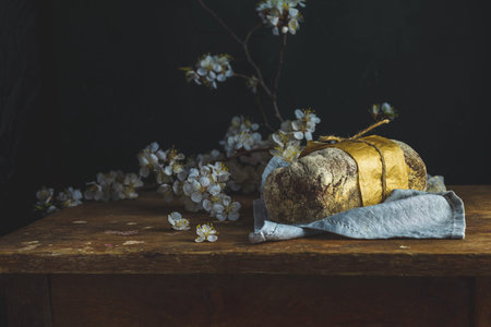 Freshly baked rye handmade breads on old wooden table with linen napkin and apricot tree blossom...
