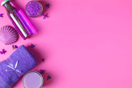 Spa products. Lavender bath salts, viola flowers, soap, cosmetic cream and towel. Violet purple concept. Flat lay on pink background, top view.の写真素材