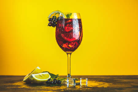 Cold red cocktail with blackcurrant, lemon, mint and ice in tall glass on yellow background. Summer drinks and alcoholic cocktails. Alcoholic cocktail Blackcurrant mojitoの写真素材