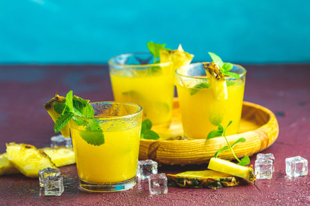 Cold cocktail with squeezed pineapple juice, lime, mint and ice in glasses on concrete surface...