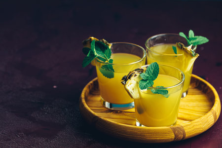 Cold cocktail with squeezed pineapple juice, lime and mint in glasses on concrete surface table....