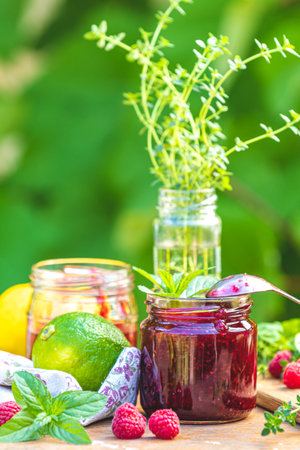 Raspberry jam and fresh raspberry on a rustic wooden table outdoors. Sunny day, green leaves...