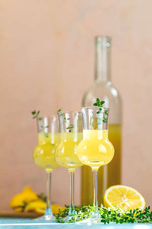 Limoncello with thyme in grappas wineglass with water drops on light concrete table. Artistic still life on light background with sunny light.の写真素材