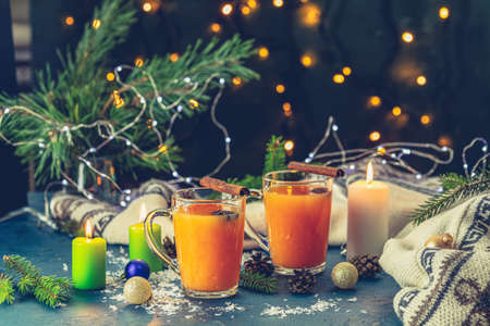 Christmas and New Year composition. Two cup of hot spicy tea with sea buckthorn, cinnamon and star anise, branches of pine and spruce, candles and holiday decor, bokeh, dark backgroundの写真素材
