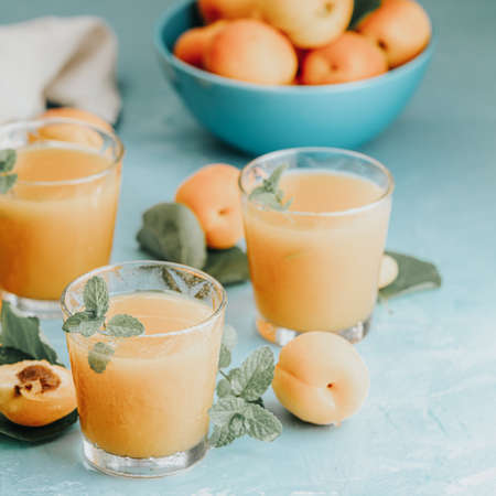 Glass of fresh healthy apricot or peach smoothie or juice on light blue concrete surface table. Sunny light. Shallow depth of the field, close up, copy space for you textの写真素材