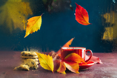 Red in white dotted cup of hot tea. Autumn teatime composition on dark background with colored...