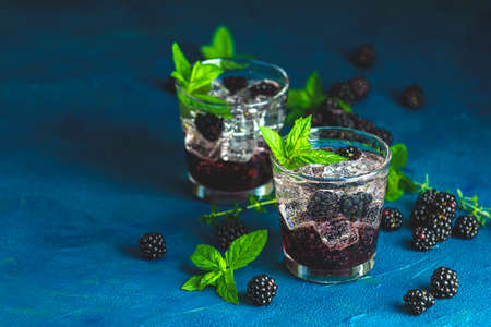 Cold summer berry drink with blackberries. Refreshing summer drink with syrup, blackberry and ice on dark blue concrete backgroundの写真素材