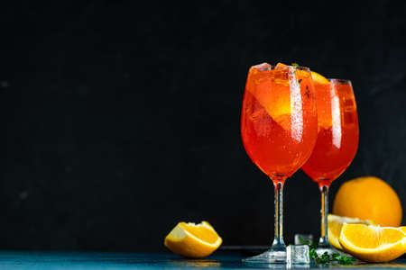 Two Aperol spritz cocktail in big wine glass with oranges, summer Italian fresh alcohol cold drink. Dark bar counter background with tools, summer mood concept, selective focusの写真素材