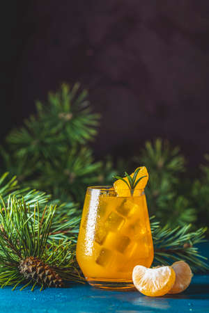 Yellow orange cocktail with tangerine and rosemary in glass on dark blue concrete background decorated pine branches with cones, close up.の写真素材