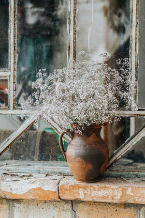 Beautiful retro still life with wild flowers in clay jug on windowsill of an old window. Close up, shallow depth of the field, copy space for text.の写真素材