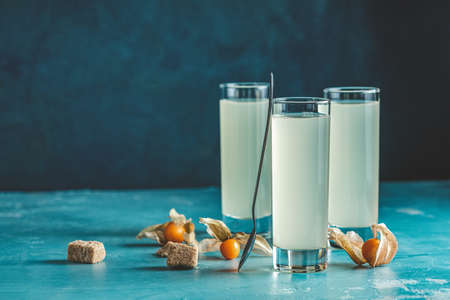 Alcoholic cocktail with Ouzo greek anise brandy or Arabic alcohol drink Raki in highball glass, decorated Physalis peruviana and brown sugar on blue concrete surface.の写真素材