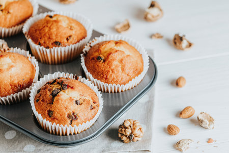 Vanilla caramel muffins in paper cups on white wooden background. Delicious cupcake with raisins,...