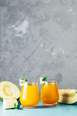 Yellow orange cocktail with melon and mint in glass on blue concrete background, close up. Summer drinks and alcoholic cocktails. Alcoholic or detox cocktailの写真素材