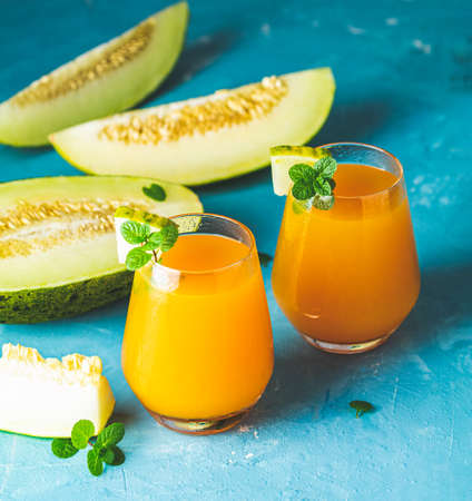 Yellow orange cocktail with melon and mint in glass on blue concrete background, close up. Summer drinks and alcoholic cocktails. Alcoholic or detox cocktailの写真素材