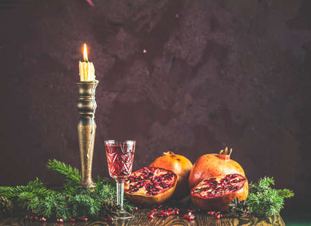 Greeting food Christmas and New Year composition. Vintage glass of pomegranate drink surrounded  pine branches and festive candles, dark background. Close up, shallow depth of the field.の写真素材