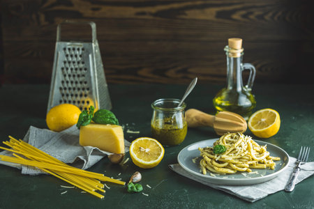 Spaghetti pasta bucatini with pesto sauce and parmesan. Italian traditional perciatelli pasta by genovese pesto sauce in gray dish served with ingredients on dark green concrete table.の写真素材