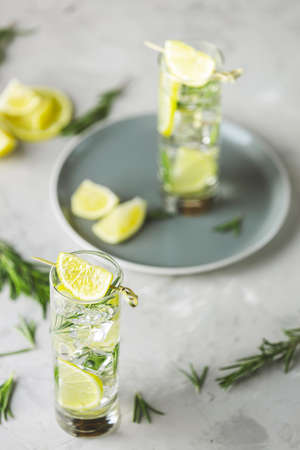 Refreshing lemon lime drink with ice cubes in glass goblets against a light gray background. Summer fresh lemon soda cocktail with rosemary, selective focus.の写真素材