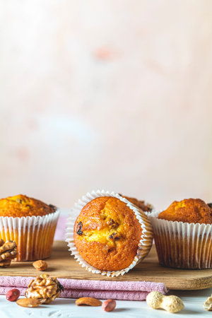 Vanilla caramel muffins in paper cups on white wooden background. Delicious cupcake with raisins,...
