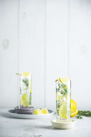 Refreshing lemon lime drink with ice cubes in glass goblets against a light gray background. Summer fresh lemon soda cocktail with rosemary, selective focusの写真素材