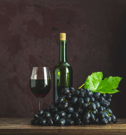 Glasses and bottles of wine and grapes on dark claret bordeaux concrete surface backgroundの写真素材