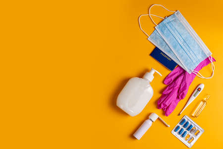 Coronavirus and travel concept. Passports, sanitizer, thermometer, medical gloves, surgical mask, sanitizer gel, blue capsules pill in blister and medical mask on yellow colored background, flat lay.の写真素材